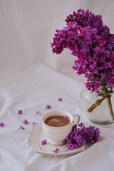 Cup of coffee with lilac flowers on a white background.