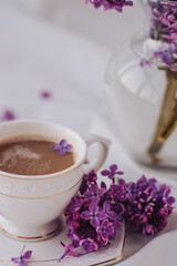 Cup of coffee with lilac flowers on a white background.
