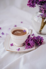 Cup of coffee with lilac flowers on a white background.