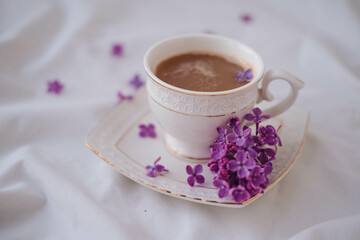 Obraz na płótnie Canvas Cup of coffee with lilac flowers on a white background.
