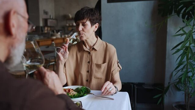 Pretty elderly couple clinking glasses of wine at lunch in cafe