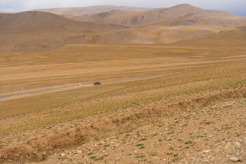 Fototapeta premium car driving through the desert. Landscape of Desert mountains against clouds sky at Ladakh, India
