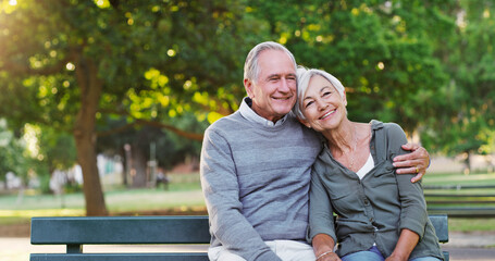 Senior couple, bench and happy outdoor in a park with love, care and support in marriage. A elderly man and woman hug in nature with a smile for quality time, healthy retirement and freedom to relax