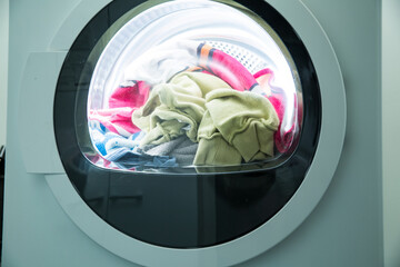 Dryer machine in a Landry room at home drying clothes. Spinning drum with load of laundry. Household chores concept