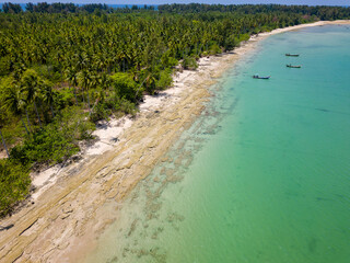 Low drone view of an empty tropical beach surrounded by palm trees (Khao Lak, Thailand)