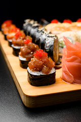 Maki rolls with salmon and tobiko calve on wooden serving board on dark table