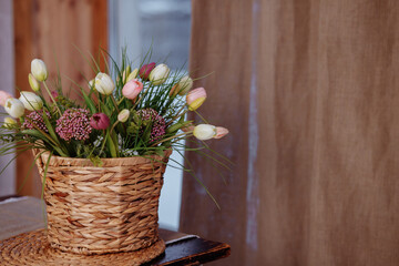 A wicker basket filled with tulips daisies against a wooden wall.