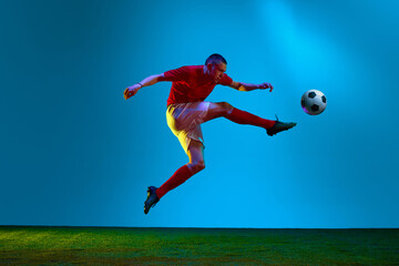 Naklejka premium Portrait with one professional football, soccer player in sportswear playing, training over field, stadium background in neon light