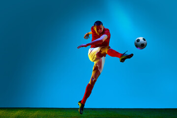 One young man, professional soccer football player training over soccer field background in neon light. Concept of action, energy, sport, team game. Sport betting © Lustre Art Group 