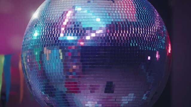 A spinning mirror disco ball flickers with multicolored lights. Disco ball close up on the background of the room. Musical and dance background of the night party.