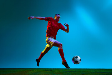 Obraz na płótnie Canvas Portrait with one professional football, soccer player in sportswear playing, training over field, stadium background in neon light. Concept of team game, sport