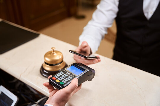Male guest paying contactless while manager holding credit card machine in hotel