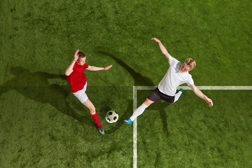 Fototapeta premium Two of football player in sports uniform and football boots playing, training with ball over green grass field background. Aerial view
