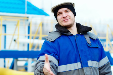 Invitation to team of professional gas workers. Young gas engineer in hardhat and winter pea coat extends his hand forward to greet. Positive attitude. Authentic Caucasian worker.