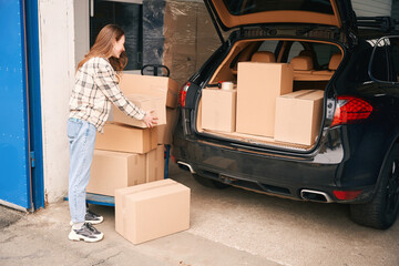 Young woman with cardboard boxes near the trunk of the car in a warehouse © Viacheslav Yakobchuk