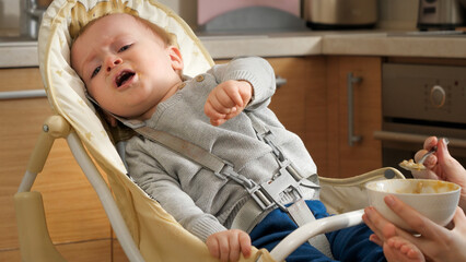 Portrait of baby crying and refusing to eat in highchair at kitchen. Concept of parenting, healthy...