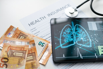 Modern social health insurance program. Tablet computer with healthcare application interface on screen. Stethoscope, x-ray image and cardiogram on wooden desk. Digital healthcare technologies