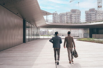 Two young businessmen outdoors walking talking and chatting