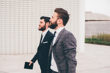 Two young elegant businessmen walking outdoors together in the streets