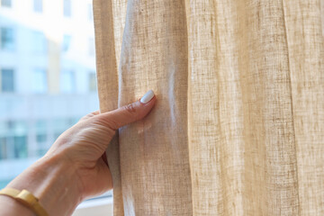 Gray linen natural curtains on window, close-up of hand touching curtains - obrazy, fototapety, plakaty