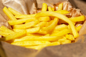 Fresh tasty fried french fries in paper bag in sunlight close up. Selective focus, defocus
