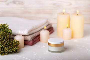 Face cream and burning candles, towels and juniper branch on light background. Concept of calmness, comfort, spa treatments. Selective focus