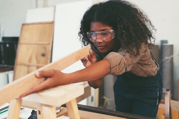 Female carpenter working in wood workshop. Female joiner wearing safety uniform and working in furniture workshop