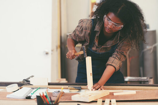 Female carpenter working in wood workshop. Female joiner wearing safety uniform and working in furniture workshop