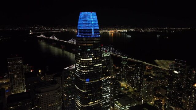 Aerial view of Salesforce Tower and Bay Bridge over water surface in background. Night shot of modern city. San Francisco, California, USA