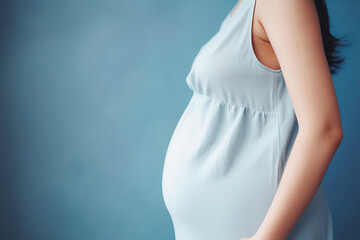 A pregnant caucasian woman in blue dress strokes her belly on blue background. Place for text. Copy space. Waiting for the birth of a child. High quality photo - obrazy, fototapety, plakaty