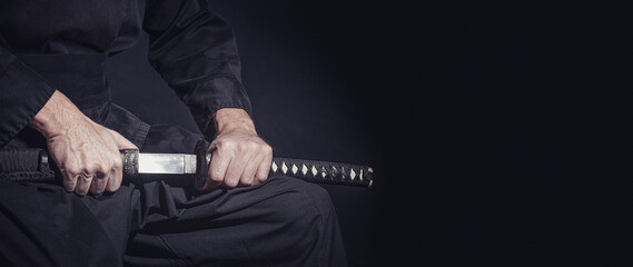 The samurai holding a Japanese katana sword, banner. Photo of a warrior dressed in black clothes in...