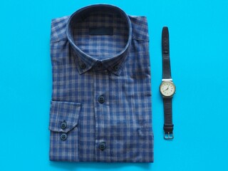 Mens shirt and wristwatch on a blue background. Classic mens fashion. The beginning of a new working day