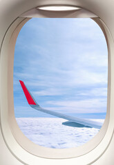 View from inside airplane cabin of Aircraft wing while flying above fluffy clouds inside of plane window frame