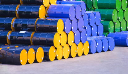 Piles of many various 200-litre oil drums stacked on the patio outside of industrial building in...