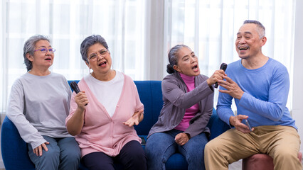 Happy senior Asian friends singing karaoke on the sofa in the living room with happy smiling face. Elderly people singing karaoke. Friends singing karaoke at home