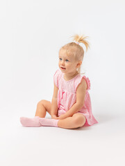 A 1-2-year-old toddler girl in a pink dress enthusiastically looks at something and sits on the...