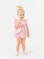 A 2-year-old blonde toddler girl in a pink dress points with her index finger and looks expressively at a white background.