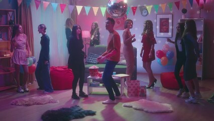 A group of friends at a party. Children dance in a room with a spinning disco ball. The girl in black feels awkward, modestly dancing next to the guy. On the table are paper cups, pizza and popcorn.