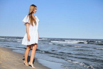 Fototapeta na wymiar Happy smiling beautiful woman is walking on the ocean beach in a white summer dress.