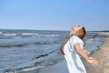 Fototapeta na wymiar Happy, beautiful woman on the ocean beach standing in a white summer dress, open arms.