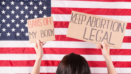 Young woman protester holds cardboard with Keep Abortion Legal and Bans Of My Body signs against...