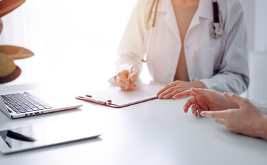 Doctor and patient discussing current health examination while sitting at the desk in clinic office. The focus is on female patient's hands, close up. Perfect medical service and medicine concept.