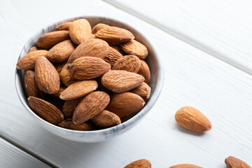Fresh almonds in a bowl on white wooden background. Bowl of almonds on wooden background. Close-up. 