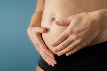 Very close up view of pregnant woman holding her belly gently during first months of pregnancy. Pregnancy first trimester - week 18. Side angle view. Blue background. Bright shot.
