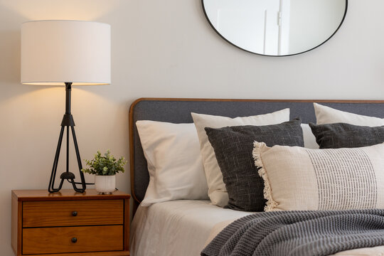 Relaxing Bedroom Detail Of Bed With Gray And White Linen Textured Bedding, Decorative Wood Side Table With Wire Lamp, And Round Mirror.