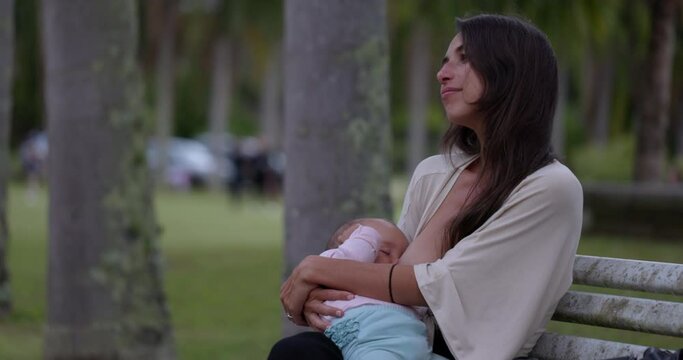 Mother breastfeeding in busy park on sunny summer day