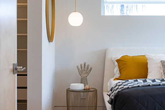 Clean Lines Of A Modern Bedroom With Hanging Globe Light Over Wire End-table, Bed With White, Gold And Blue Accents, Gold Rim Mirror, And Peek Into Closet.