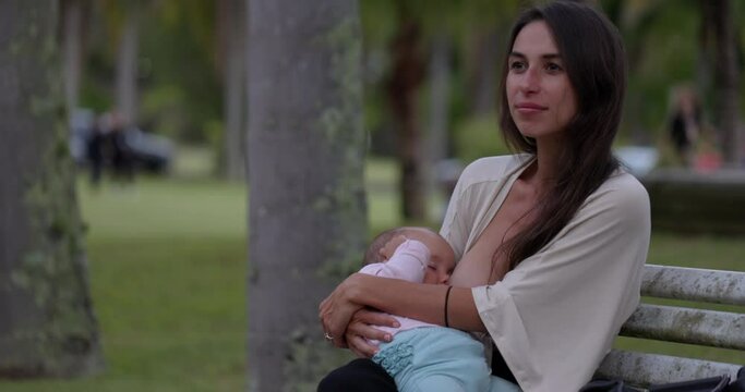 Mother breastfeeding on park bench in summer - wide shot