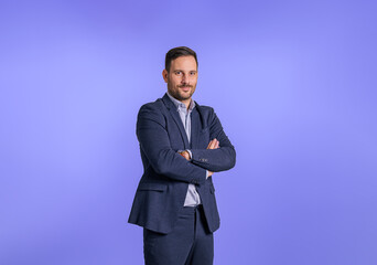 Portrait of handsome male professional executive wearing elegant blue suit and posing confidently. Smiling businessman with arms crossed looking at camera and standing against blue background - obrazy, fototapety, plakaty