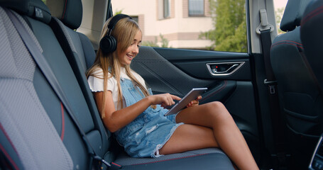 Pretty smiling caucasian girl with tablet sitting in car. Girl passenger in car reading digital tablet.